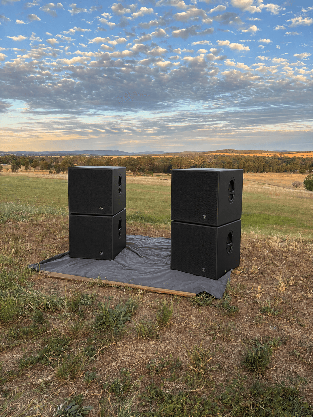 Four Mackie subwoofers stacked in pairs at sunset