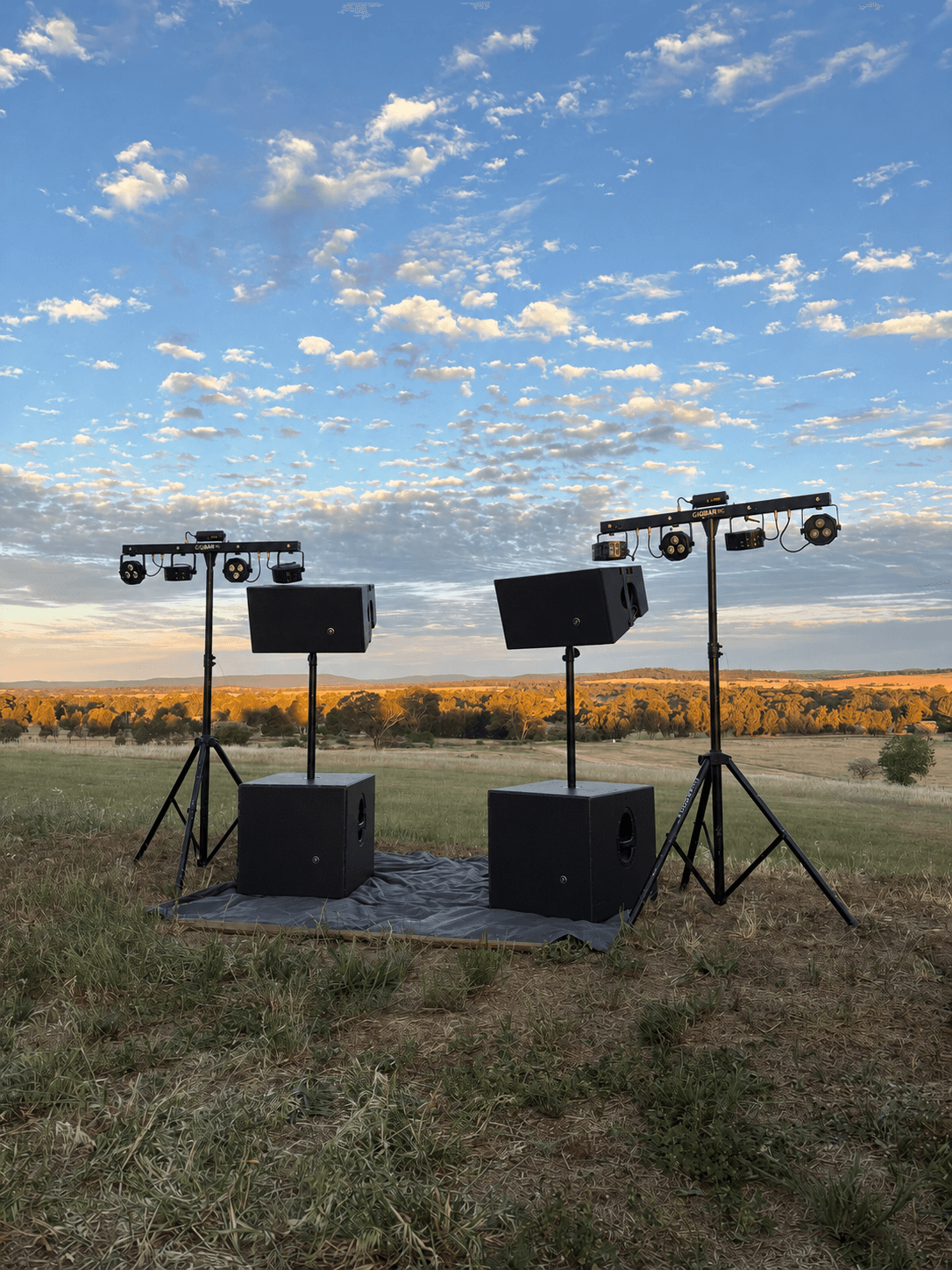 Full rig at golden hour: two Mackie HDA tops on stands, two subwoofers and two GigBAR lighting bars